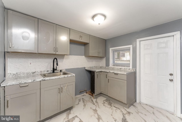 kitchen with gray cabinets, sink, light stone countertops, and backsplash