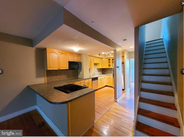 kitchen featuring light hardwood / wood-style flooring, kitchen peninsula, backsplash, sink, and black appliances