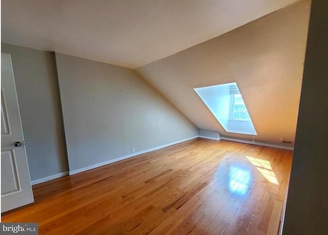 additional living space with wood-type flooring and vaulted ceiling with skylight