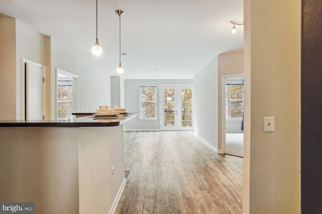 hallway with plenty of natural light, light hardwood / wood-style floors, and french doors