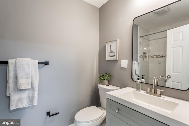 bathroom featuring toilet, vanity, and tiled shower