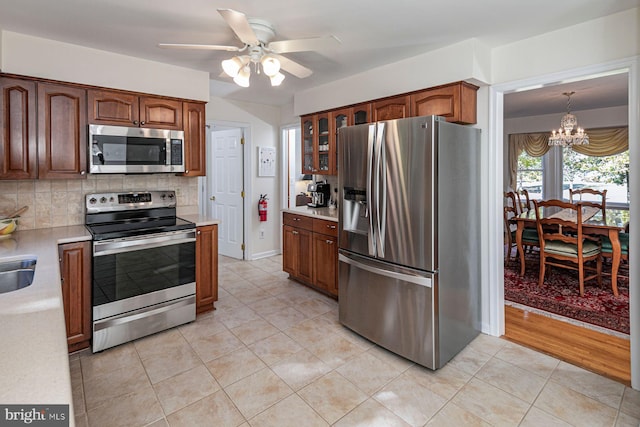 kitchen featuring appliances with stainless steel finishes, light wood-type flooring, ceiling fan with notable chandelier, backsplash, and pendant lighting