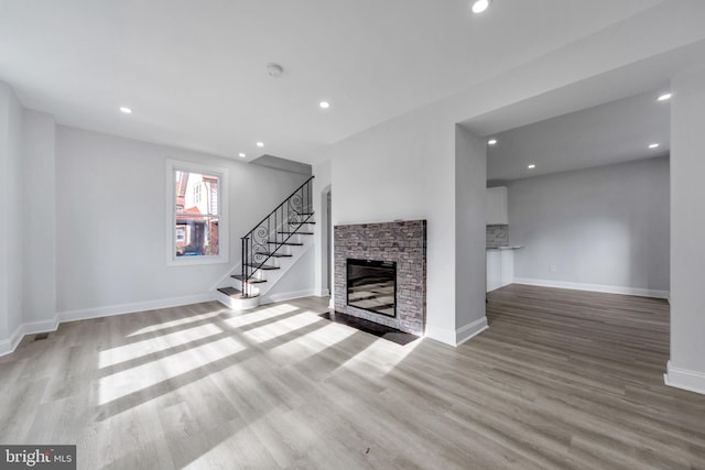 unfurnished living room with a stone fireplace and light wood-type flooring