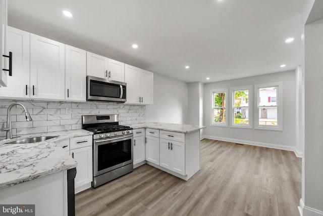 kitchen with kitchen peninsula, white cabinets, sink, light hardwood / wood-style floors, and stainless steel appliances