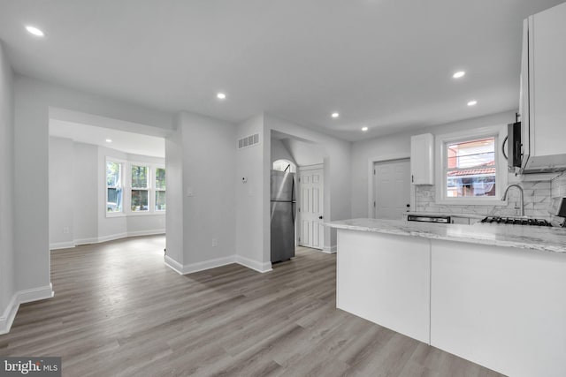 kitchen with light hardwood / wood-style floors, white cabinetry, light stone counters, and appliances with stainless steel finishes