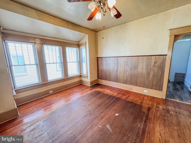 empty room with hardwood / wood-style floors, wooden walls, and ceiling fan