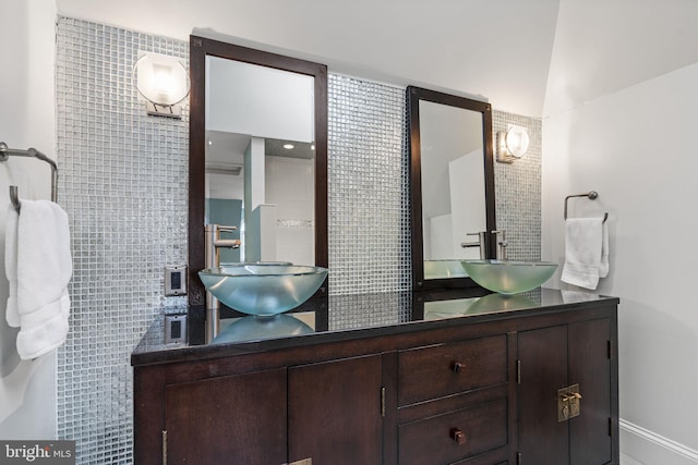 full bath featuring double vanity, tile walls, baseboards, and a sink