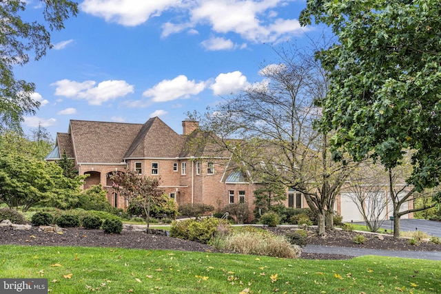 view of home's exterior featuring a chimney, brick siding, aphalt driveway, and a yard