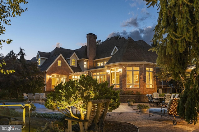 rear view of house featuring a patio, a chimney, and brick siding