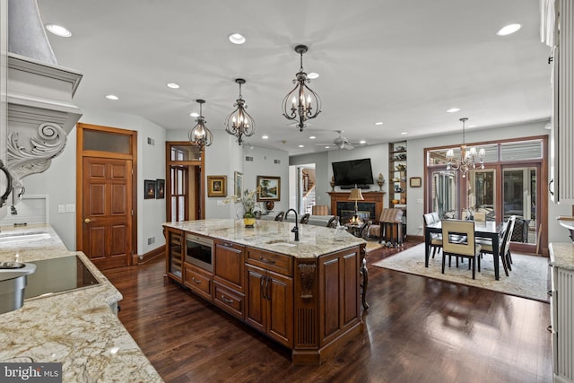 kitchen with a center island with sink, stainless steel microwave, light stone countertops, dark wood-type flooring, and pendant lighting