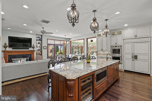 kitchen with a kitchen breakfast bar, built in appliances, light stone counters, and beverage cooler