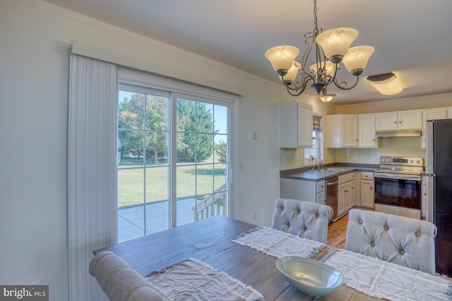 kitchen with tasteful backsplash, appliances with stainless steel finishes, sink, white cabinetry, and decorative light fixtures