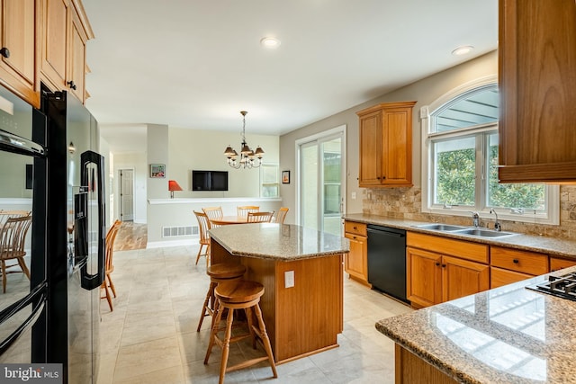 kitchen featuring a center island, black dishwasher, sink, hanging light fixtures, and a notable chandelier