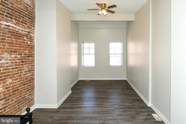 empty room featuring ceiling fan, brick wall, and dark hardwood / wood-style flooring