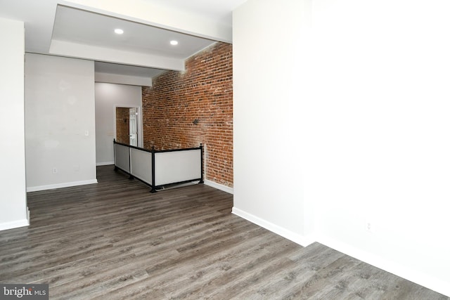 empty room with dark wood-type flooring, beam ceiling, and brick wall