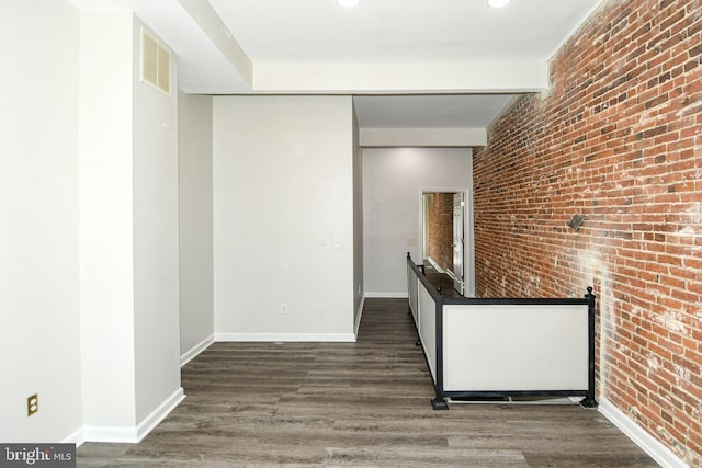 hall with brick wall, beam ceiling, and dark wood-type flooring