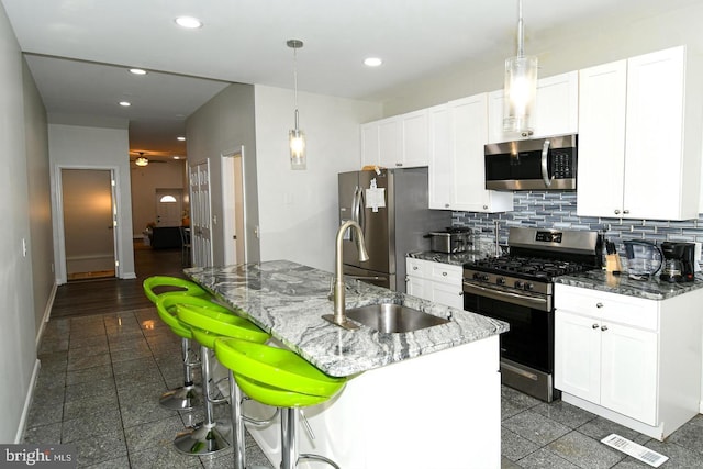 kitchen featuring white cabinets, tasteful backsplash, an island with sink, appliances with stainless steel finishes, and dark stone counters