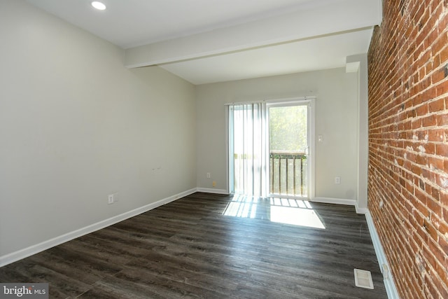 empty room featuring brick wall, beamed ceiling, and dark wood-type flooring