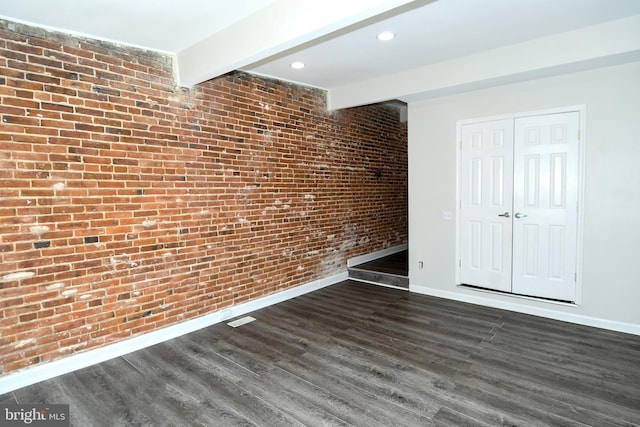 spare room featuring dark hardwood / wood-style floors, beamed ceiling, and brick wall