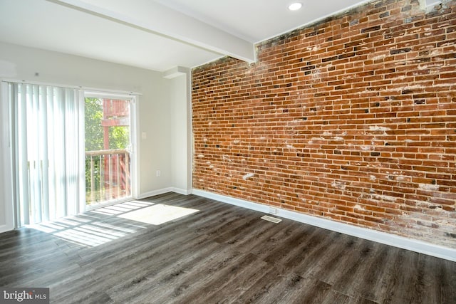 spare room with brick wall, beamed ceiling, and dark hardwood / wood-style flooring