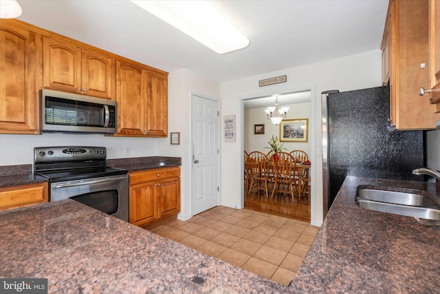 kitchen with appliances with stainless steel finishes, sink, hanging light fixtures, light tile patterned floors, and an inviting chandelier