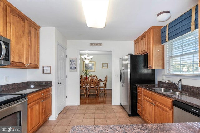 kitchen featuring light tile patterned floors, appliances with stainless steel finishes, dark stone countertops, a notable chandelier, and sink