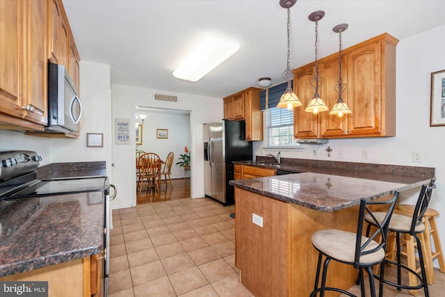 kitchen featuring a kitchen bar, kitchen peninsula, hanging light fixtures, stainless steel appliances, and light tile patterned floors