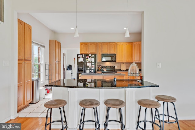 kitchen featuring light hardwood / wood-style flooring, kitchen peninsula, dark stone counters, black appliances, and pendant lighting