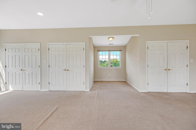 unfurnished bedroom with multiple closets, light carpet, and ceiling fan