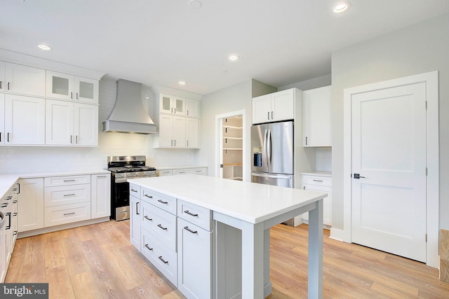 kitchen with white cabinets, light hardwood / wood-style floors, a kitchen island, custom range hood, and appliances with stainless steel finishes