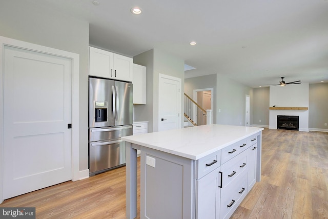 kitchen with stainless steel refrigerator with ice dispenser, ceiling fan, light hardwood / wood-style flooring, white cabinets, and a kitchen island