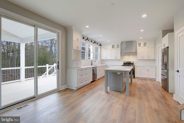 kitchen featuring custom exhaust hood, stainless steel appliances, a kitchen island, light hardwood / wood-style flooring, and white cabinetry