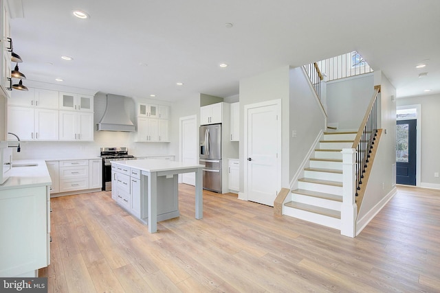 kitchen featuring light wood-type flooring, custom exhaust hood, stainless steel appliances, a center island, and white cabinetry