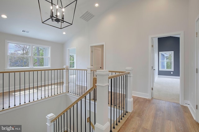 hallway with a notable chandelier, high vaulted ceiling, and light hardwood / wood-style flooring