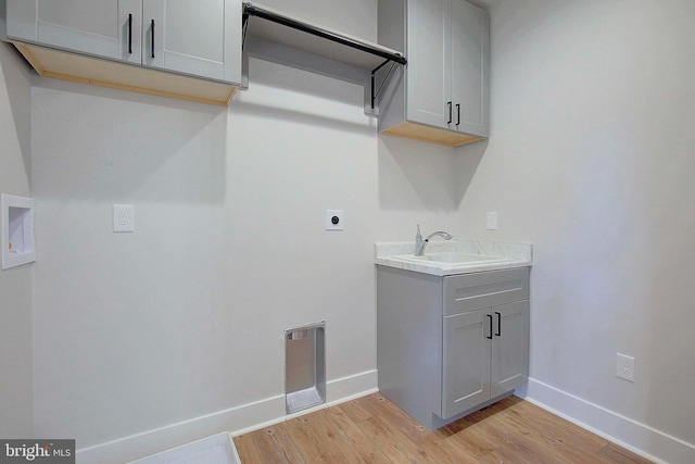 laundry room with hookup for an electric dryer, cabinets, light wood-type flooring, and sink