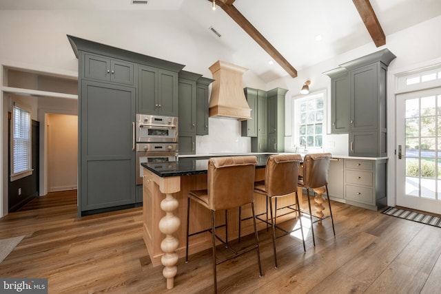 kitchen with gray cabinetry, beamed ceiling, a kitchen island, and hardwood / wood-style floors