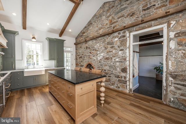 kitchen with sink, a center island, hardwood / wood-style floors, dark stone countertops, and beam ceiling