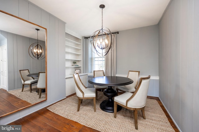 dining space featuring hardwood / wood-style flooring, wood walls, a chandelier, and built in shelves