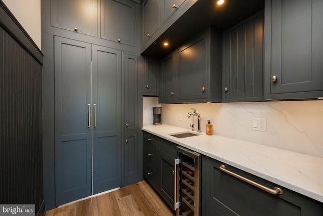 kitchen with tasteful backsplash, beverage cooler, light stone countertops, light hardwood / wood-style floors, and sink