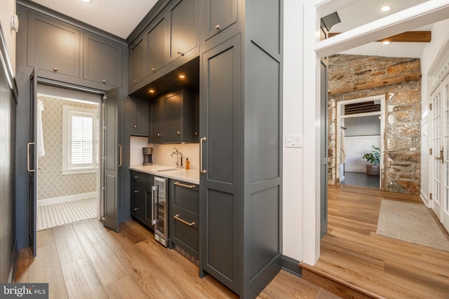 kitchen featuring sink, lofted ceiling with beams, light hardwood / wood-style flooring, and beverage cooler