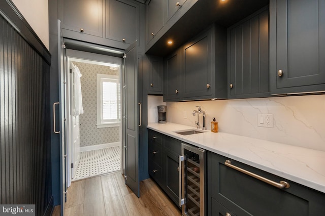 kitchen with wine cooler, light stone counters, backsplash, light hardwood / wood-style floors, and sink