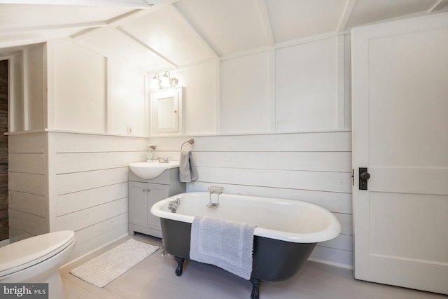 bathroom featuring a tub, toilet, hardwood / wood-style floors, vanity, and wood walls