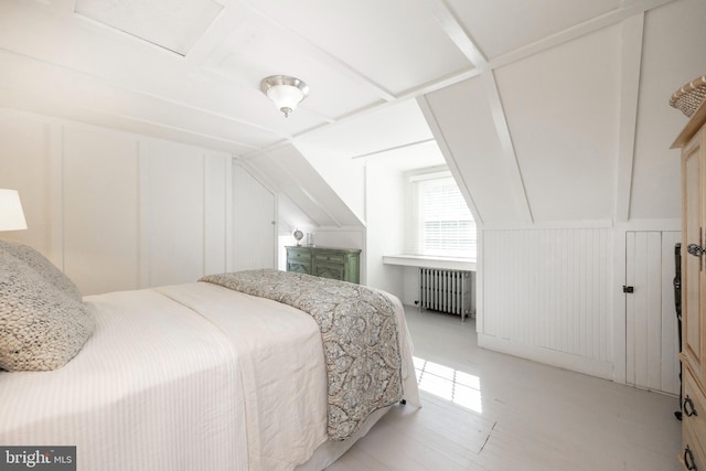 bedroom with vaulted ceiling, radiator heating unit, and light wood-type flooring