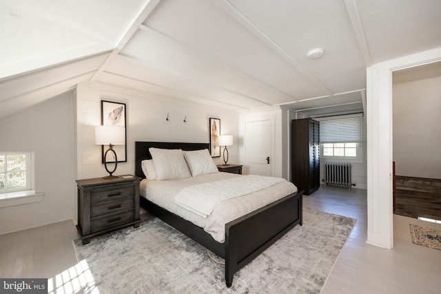 bedroom with lofted ceiling, multiple windows, light wood-type flooring, and radiator