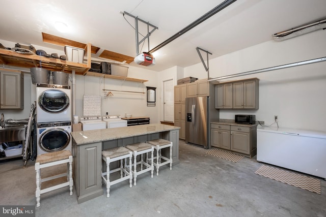 kitchen featuring a center island, stainless steel fridge, stacked washer / drying machine, light stone counters, and a breakfast bar