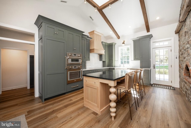 kitchen featuring hardwood / wood-style flooring, beamed ceiling, a center island, gray cabinets, and premium range hood