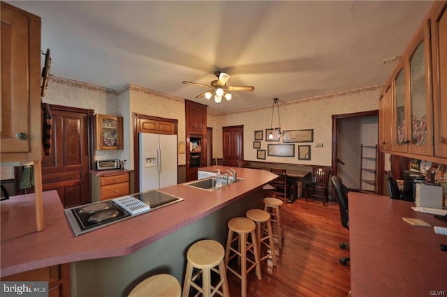 kitchen featuring dark hardwood / wood-style flooring, white fridge with ice dispenser, a breakfast bar, sink, and decorative light fixtures