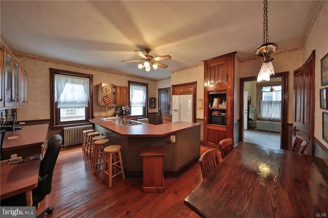 kitchen featuring kitchen peninsula, radiator heating unit, a breakfast bar, dark wood-type flooring, and white refrigerator with ice dispenser