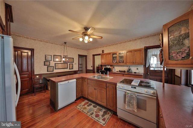 kitchen with white appliances, sink, kitchen peninsula, decorative light fixtures, and hardwood / wood-style flooring