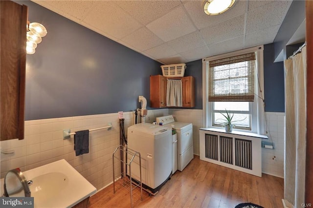 clothes washing area with radiator, tile walls, light hardwood / wood-style floors, sink, and washer and clothes dryer